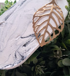 Decorative leaf-shaped object on a marble surface with green foliage in the background