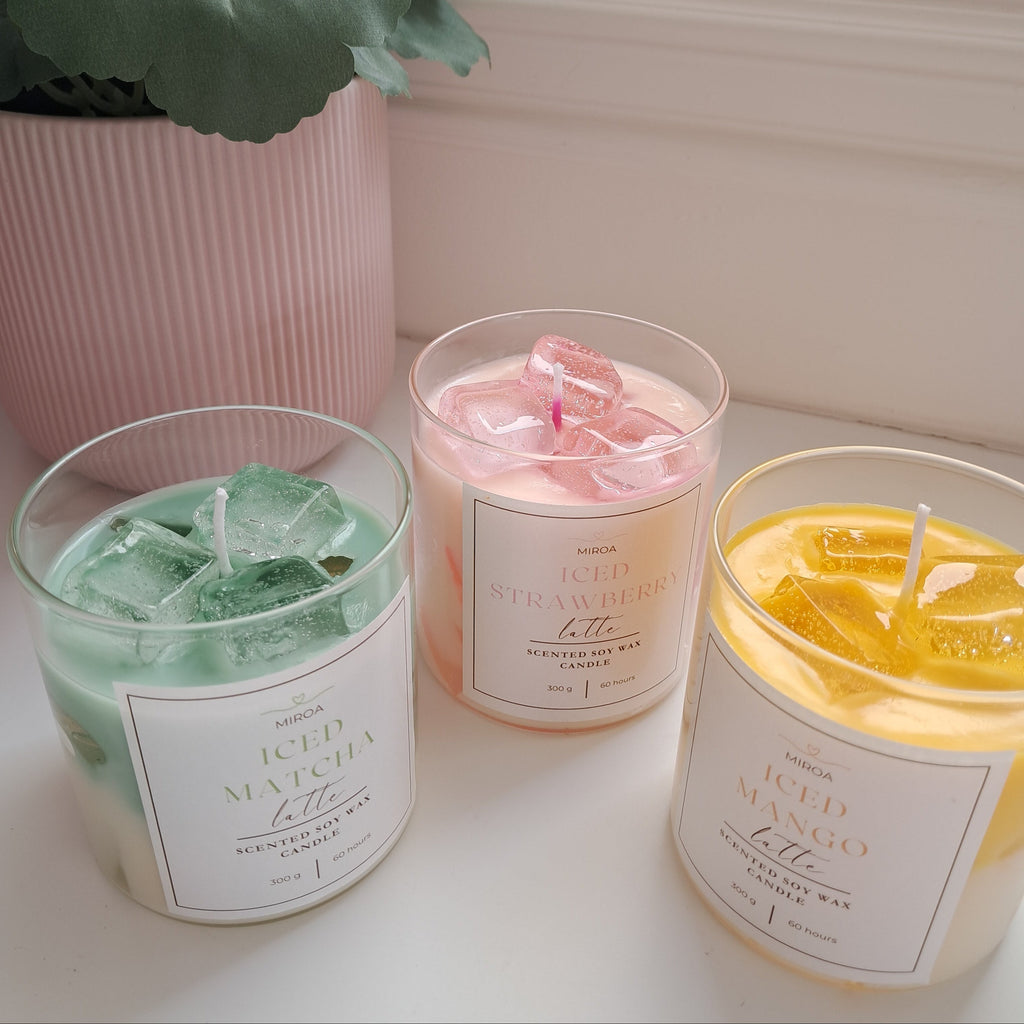 Three scented candles with colorful melts on a white surface, next to a potted plant.