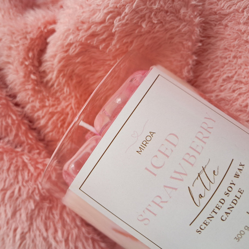 Scented candle labeled 'ICED STRAWBERRY LATTÉ' on a pink textured surface
