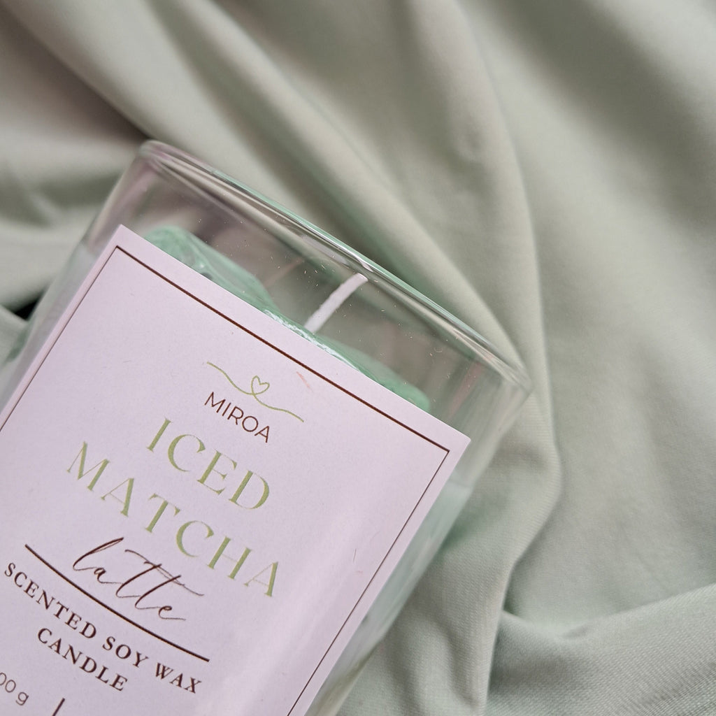 Candle labeled 'ICED MATCHA Latte' on a soft green fabric background